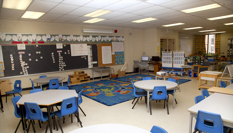 elementary school classroom with tables, chairs and carpet area