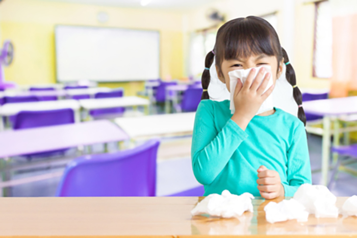young girl with tissue covering her nose and other tissues on desk in classroom