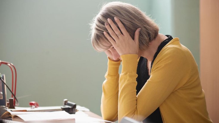 women sitting in front of a book looking down with her hands holding her head